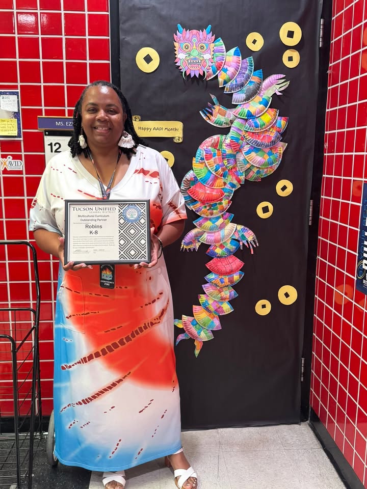 A woman in a colorful dress smiles in front of a door decorated with a dragon