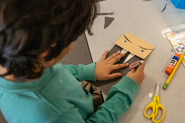 A boy creates a man in a suit out of paper bags