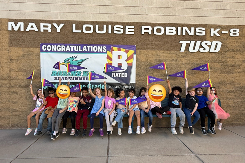 Students lined up against the front of the school holding up their purple Ruby Bridges pennants