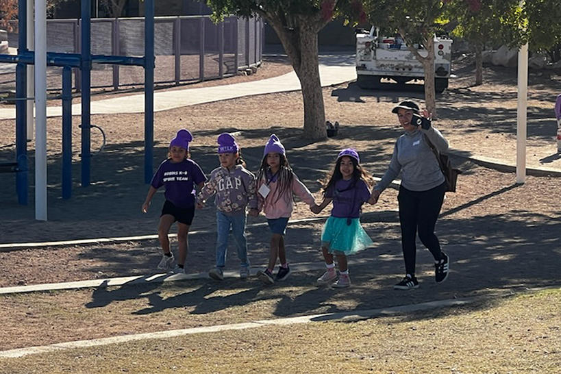Students hold hands as they walk across the playground