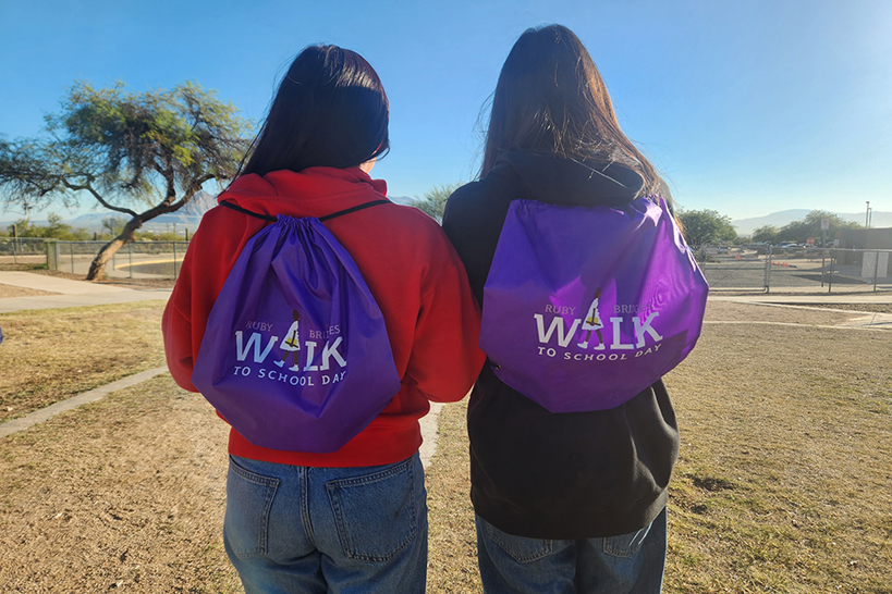 Two girls face with their backs towards the camera, showing off their purple Ruby Bridges backpacks