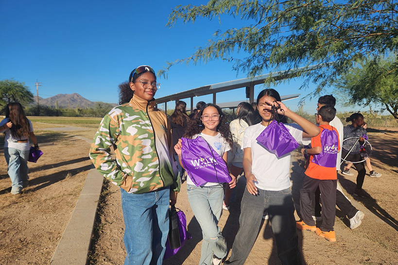 Three preteen girls smile as they show off their purple Ruby Bridges backpacks