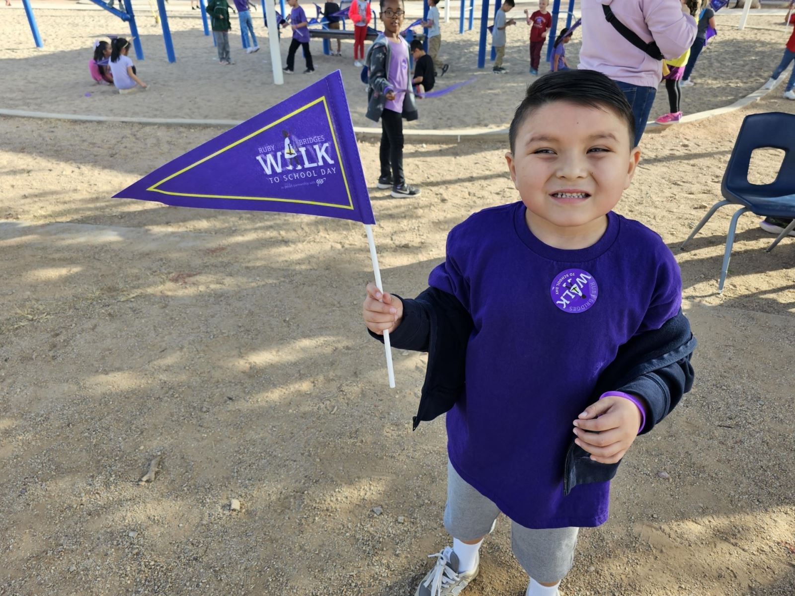 A young boy smiles while holding a purple flag that says Ruby Bridges Walk to School Day