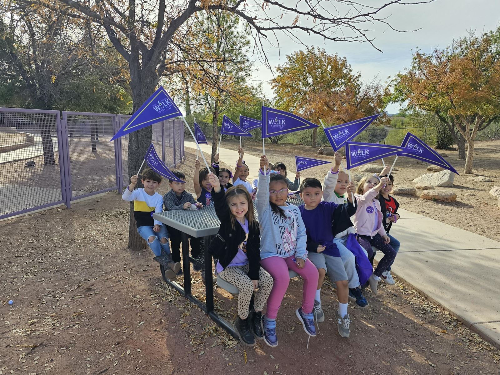 A group of students smile at a picnic table holding up their Ruby Bridges flags