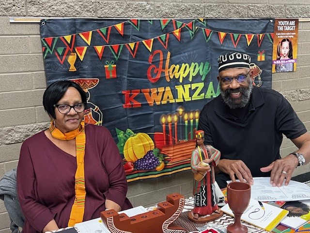 Two staff members smile at their table with Kwanzaa decorations.